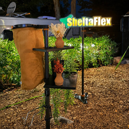 SheltaFlex Starter Set Pro mit FlexTray und FlexHook bei Nacht am Campingplatz, im Hintergrund das beleuchtete SheltaFlex Logo als stimmungsvolle Lichtinstallation.