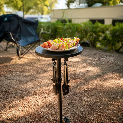 SheltaFlex TableTower aus schräger Vogelperspektive mit Grillwerkzeug sowie Campingtisch mit Fleischspießen und Gemüse – platzsparendes Outdoor-System für Camping und Vanlife.